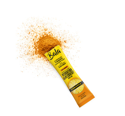An opened yellow Bala Enzyme Bala Total Body Wellness Drink Mix stick packet in pineapple flavor, with powder spilled beside it on a white background, delivers plant-based electrolytes for rapid hydration.